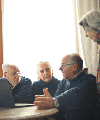 Un groupe de personnes âgées regarde un ordinateur portable autour d'une table.